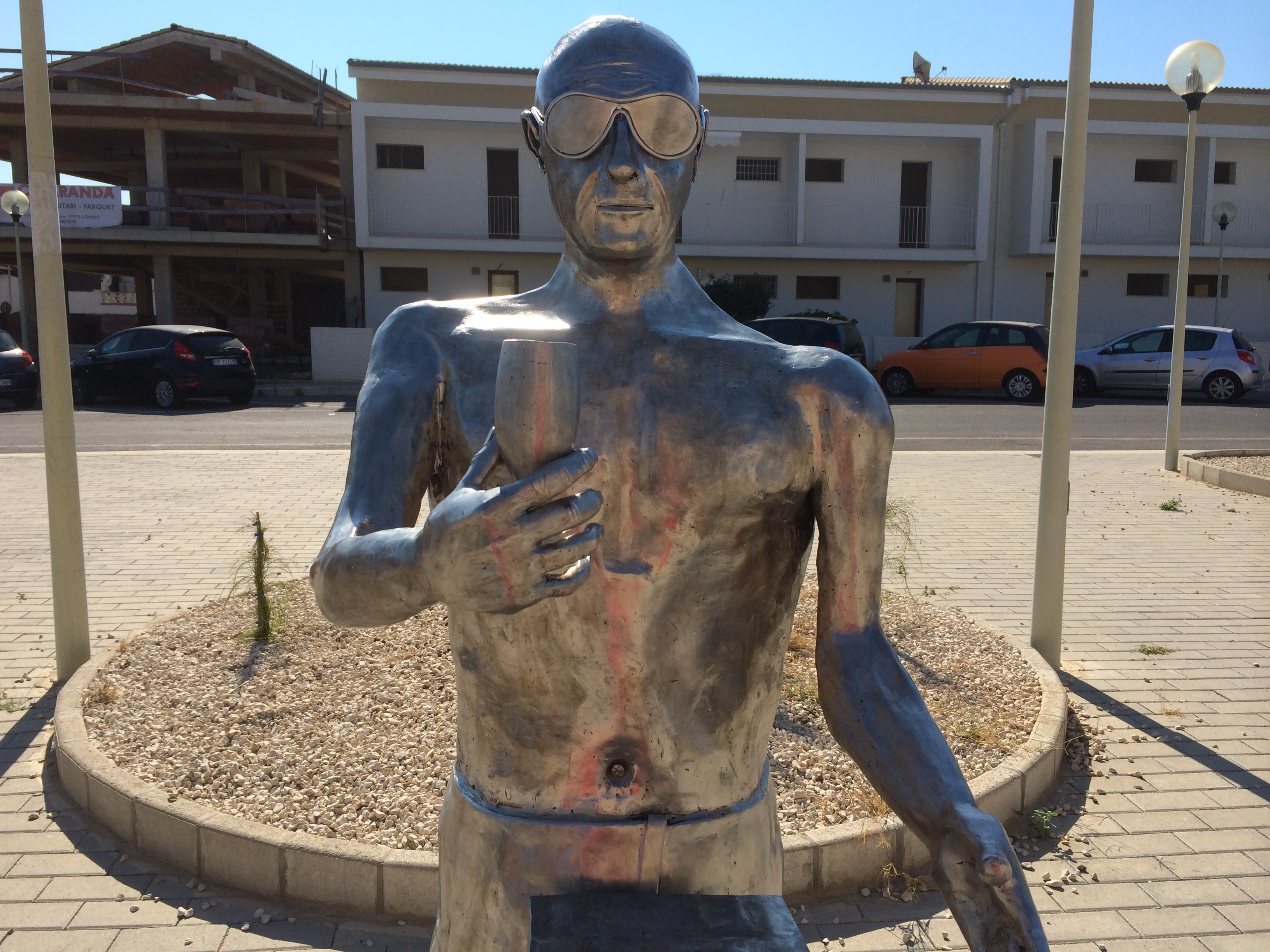 Statua in ferro di Montalbano all’entrata di P.Secca: ha occhiali da sole e calice di spumante